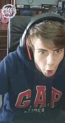 a young man wearing headphones and a gap hoodie is sticking out his tongue .