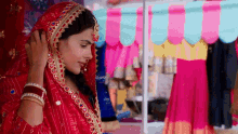 a woman in a red dress and veil is standing in front of a pink and blue striped tent .