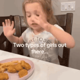 a little girl sitting at a table with a plate of nuggets and french fries