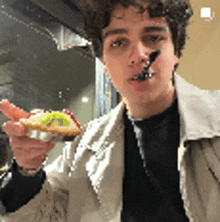 a young man is holding a piece of food in his hand with a spoon in his mouth .