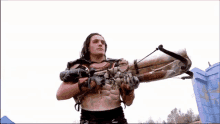 a man without a shirt is holding a large weapon in his hands .