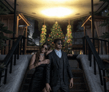 a man in a suit and a woman in a black dress are standing in front of a christmas tree