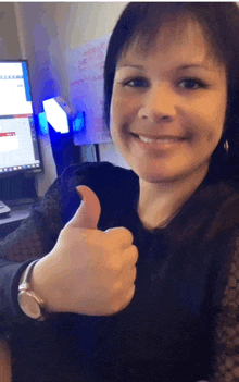 a woman giving a thumbs up in front of a computer screen