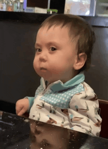 a baby is sitting at a table with a reflection of himself in the table .