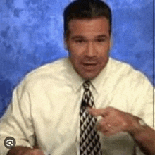 a man in a white shirt and tie is pointing at something while standing in front of a blue wall .