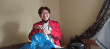 a young man in a red adidas jacket is smiling while holding a blue bag