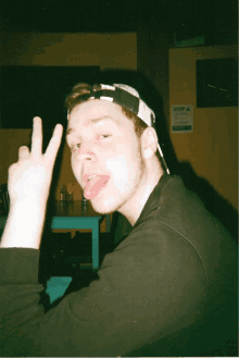 a young man making a peace sign with his tongue out in front of a sign that says stop