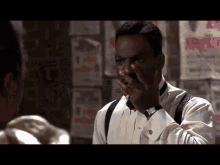 a man in a tuxedo covering his mouth with his hand in front of a wall of posters including one that says no parking