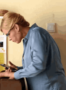 a woman wearing glasses and a blue shirt is using a cell phone