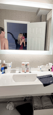 a woman is taking a picture of a man in a bathroom mirror