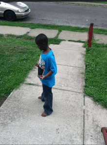 a young boy wearing a blue shirt that says ' jesus ' on it stands on a sidewalk