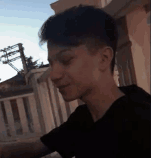 a young man in a black shirt is standing in front of a building and looking at the camera .