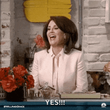 a woman in a white suit is sitting at a table laughing and says yes .
