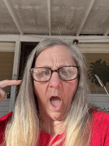 a woman wearing glasses and a red sweater makes a funny face