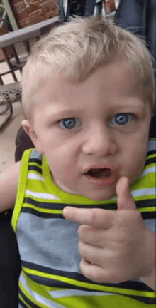 a little boy with blue eyes giving a thumbs up