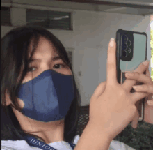 a girl wearing a blue mask is taking a selfie with her phone