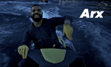 drake is smiling while riding a jet ski in the water and the word arx is above him