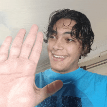 a young man in a blue shirt waves his hand in front of the camera