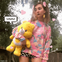 a girl wearing a pink care bears sweater holds a teddy bear