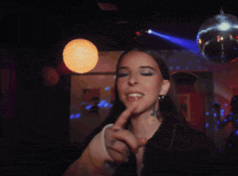 a woman is pointing at the camera with a disco ball behind her