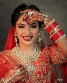 a bride in a red and gold dress is holding her hand to her face .