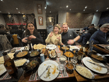 a group of people sitting around a table with plates of food and a bottle of budweiser