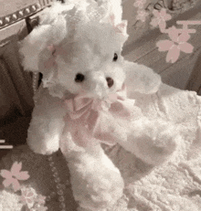 a white teddy bear with a pink bow on it is sitting on a bed .