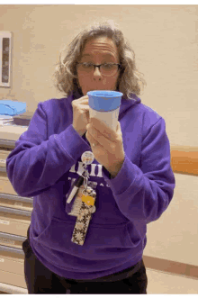 a woman in a purple sweatshirt holds a cup in her hands