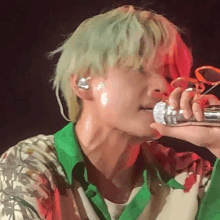 a man with green hair is holding a microphone in his hand and singing into it .