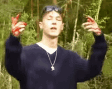 a young man with blood on his hands is standing in the woods with his eyes closed .