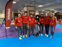 a group of people posing for a photo in front of a banner that says savana