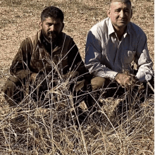 two men are kneeling down in a field of dry grass