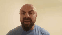 a bald man with a beard is wearing a blue shirt and making an angry face .