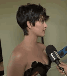 a woman is talking into a microphone while wearing a strapless black dress .