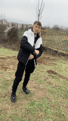 a young man wearing a black and white jacket stands in a field