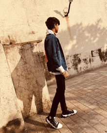 a man wearing a denim jacket and black pants is walking down a sidewalk