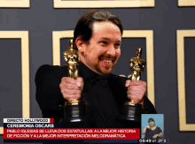 a man is holding two oscar trophies in front of a screen that says directo hollywood