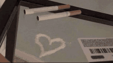 two cigarettes are laying on a table next to a heart drawn in powder .