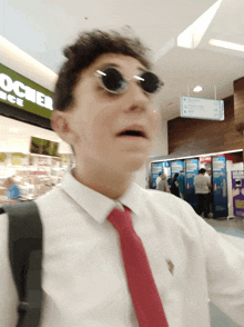 a man wearing sunglasses and a red tie stands in front of a rocher ice sign