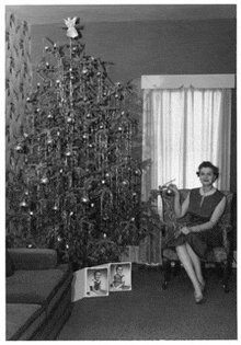 a woman is sitting in front of a christmas tree holding a christmas ornament