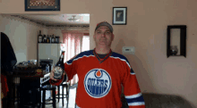 a man in a red oilers jersey holds a bottle of beer