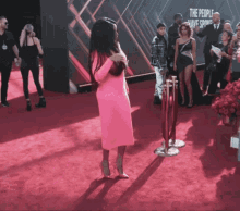 a woman in a pink dress is standing on a red carpet with a sign that says the people have spoken