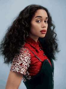 a woman with curly hair wearing a red top and green overalls