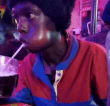 a man in a red and blue shirt drinks through a straw from a cup