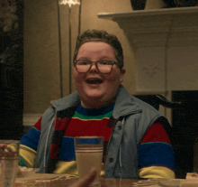 a boy wearing glasses sits at a table with a cup of milk