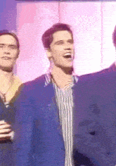 a man in a blue jacket is laughing while standing next to another man in a striped shirt .