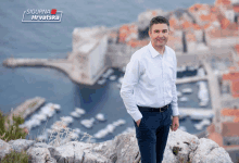 a man in a white shirt stands on top of a rocky hill in front of a sign that says sigurna hrvatska