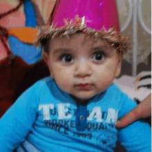 a baby wearing a party hat and a blue shirt is being held by a person .