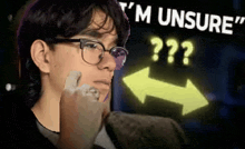 a man wearing glasses is looking at a neon sign that says `` i 'm unsure '' .