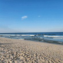 a sandy beach with a blue sky and waves crashing on the shore